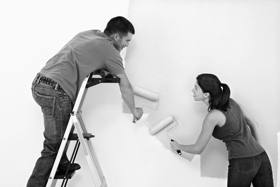 Attractive young adult couple painting interior wall of house.